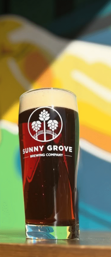 Sunny Grove Beer glass on a table with colorful mural background